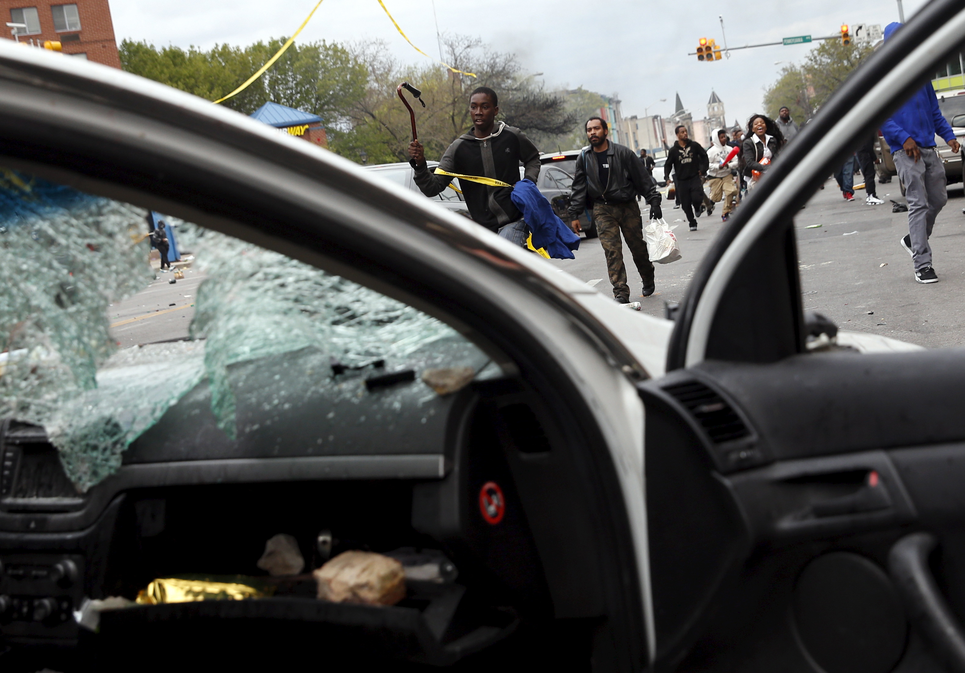 Demonstrators run by a damaged Baltimore police vehicle during clashes in Baltimore