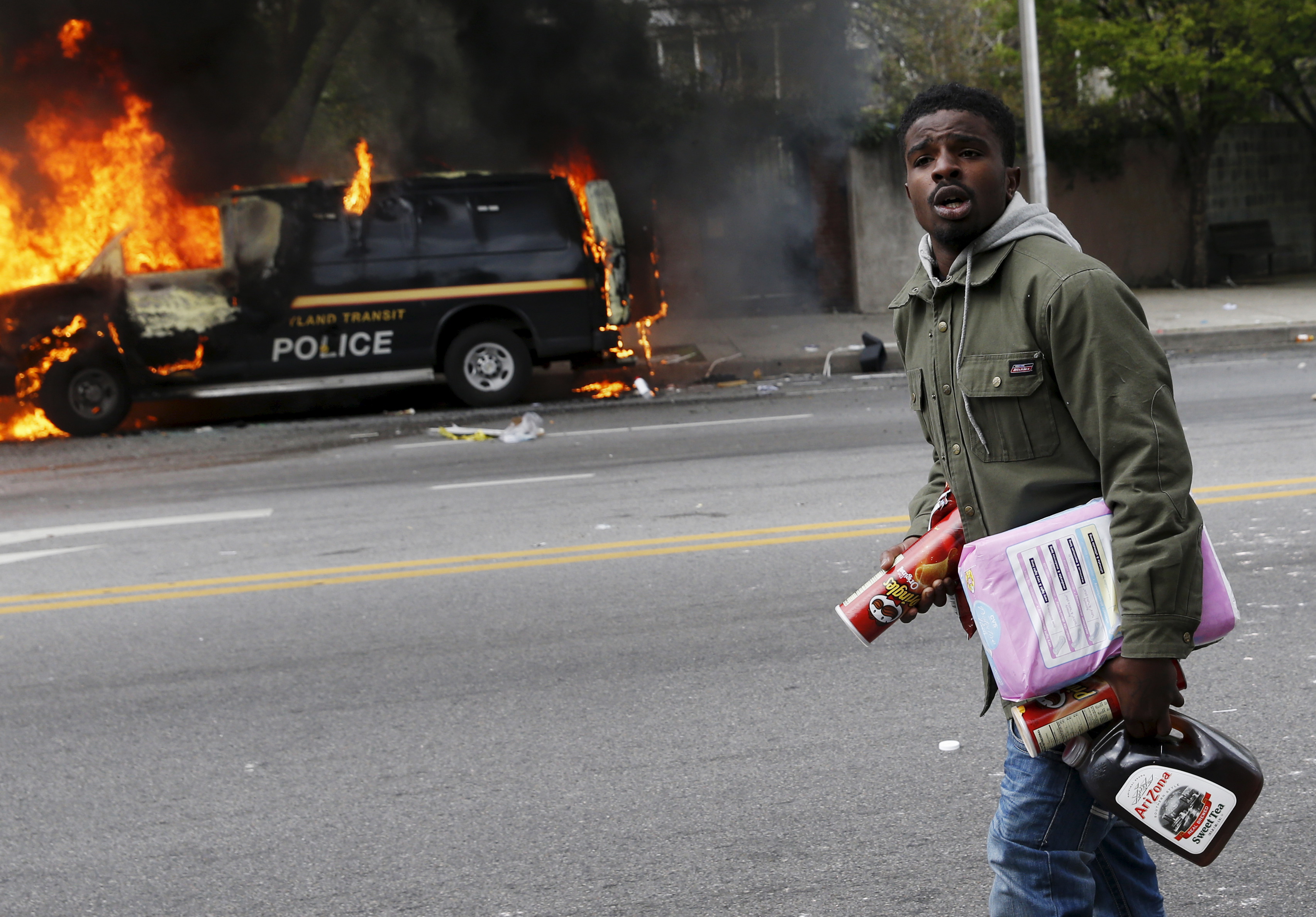 A man with looted goods walks by burned vehicles in Baltimore