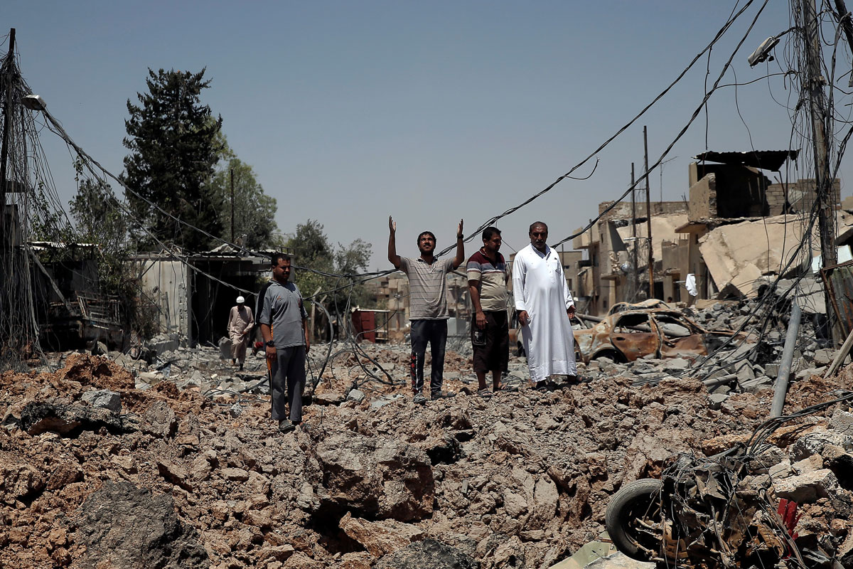 A civilian raises his hands to the sky as he and others stand among debris near the frontline in western Mosul