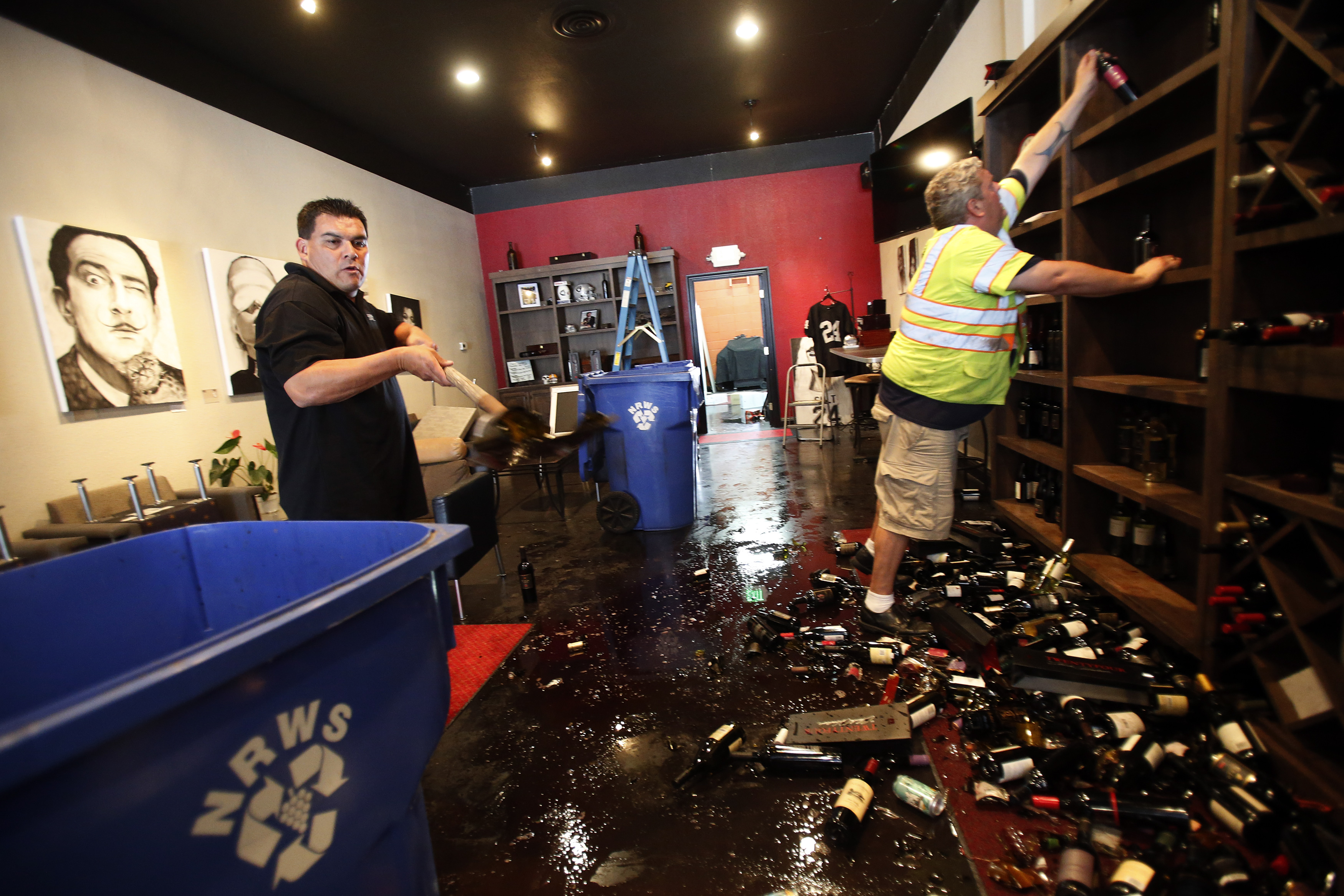 Rick Ruiz and Tyler Paradise gather broken wine bottles from the floor of their Cult Following Wine Bar after an earthquake in Napa, California