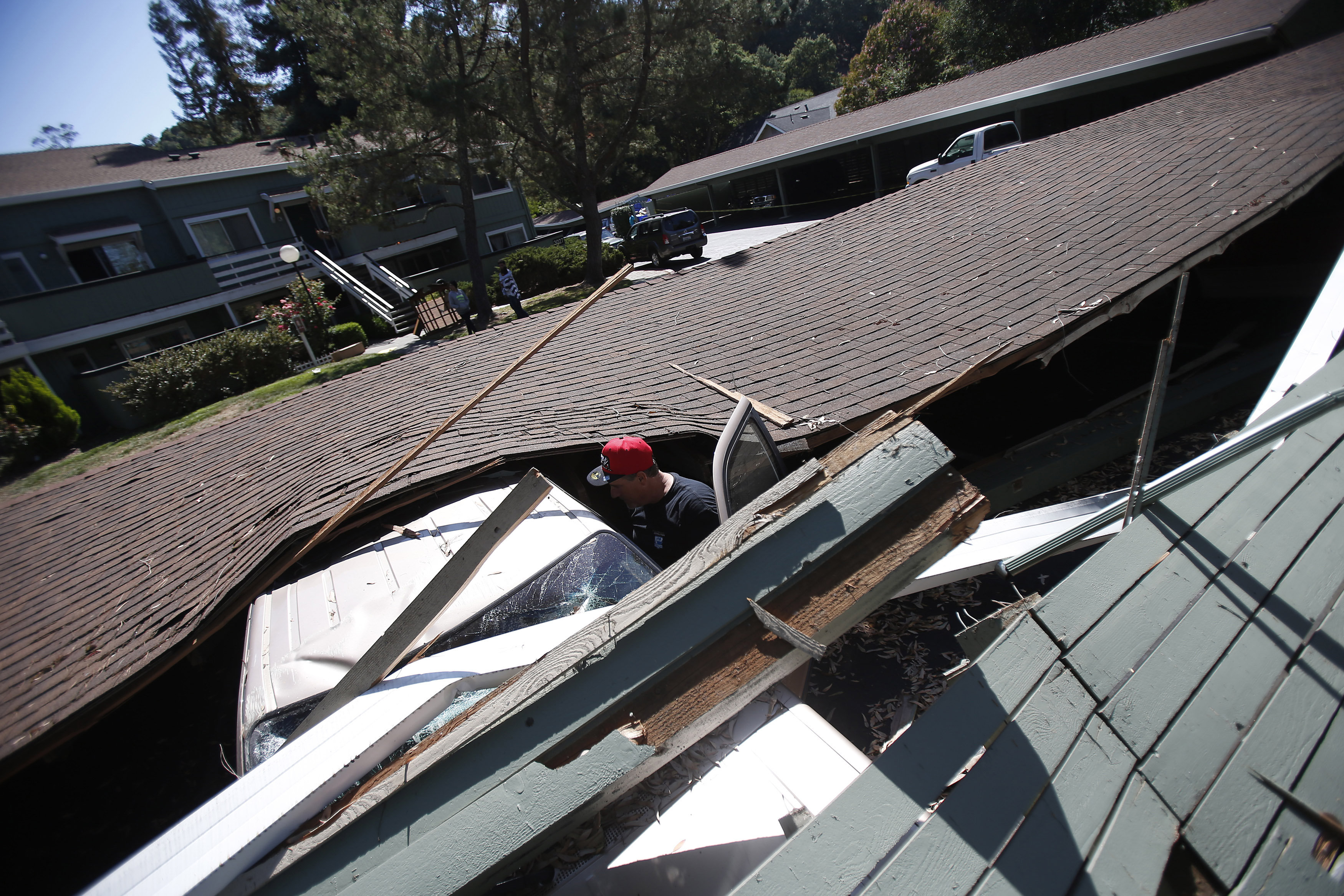 Man surveys the damage on a vehicle crushed by a collapsed parking structure in Napa