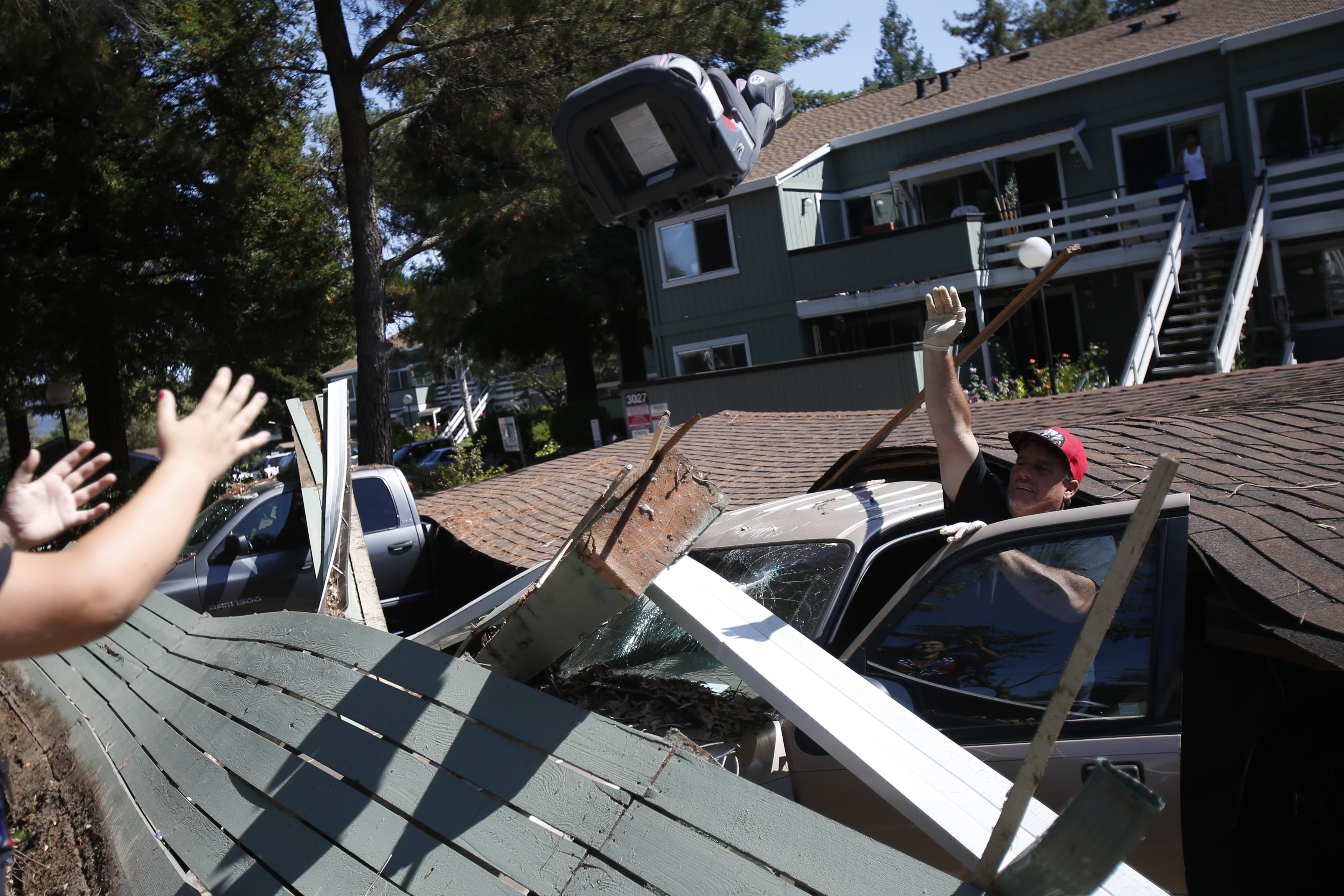 Man removes a car seat from a vehicle crushed by a collapsed parking structure in Napa