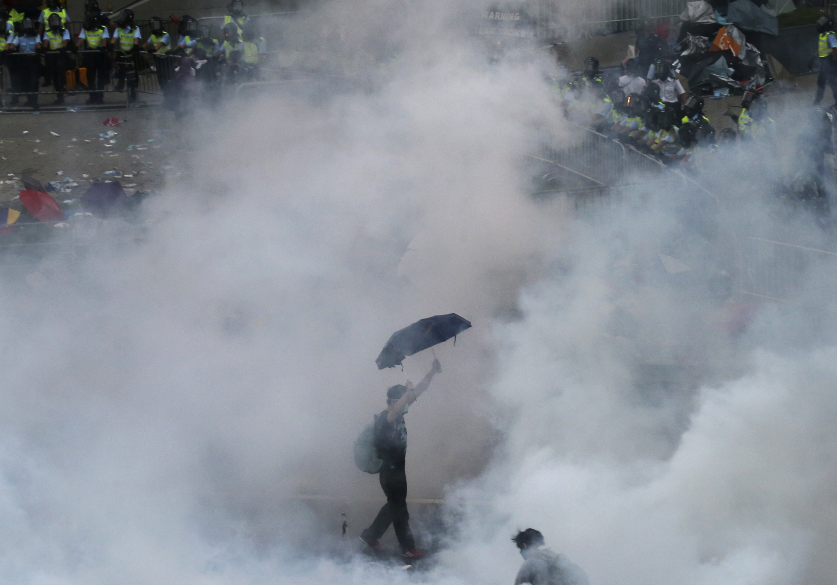 A protester walks in tear gas fired by riot policemen after thousands of protesters blocking the main street to the financial Central district outside the government headquarters in Hong Kong