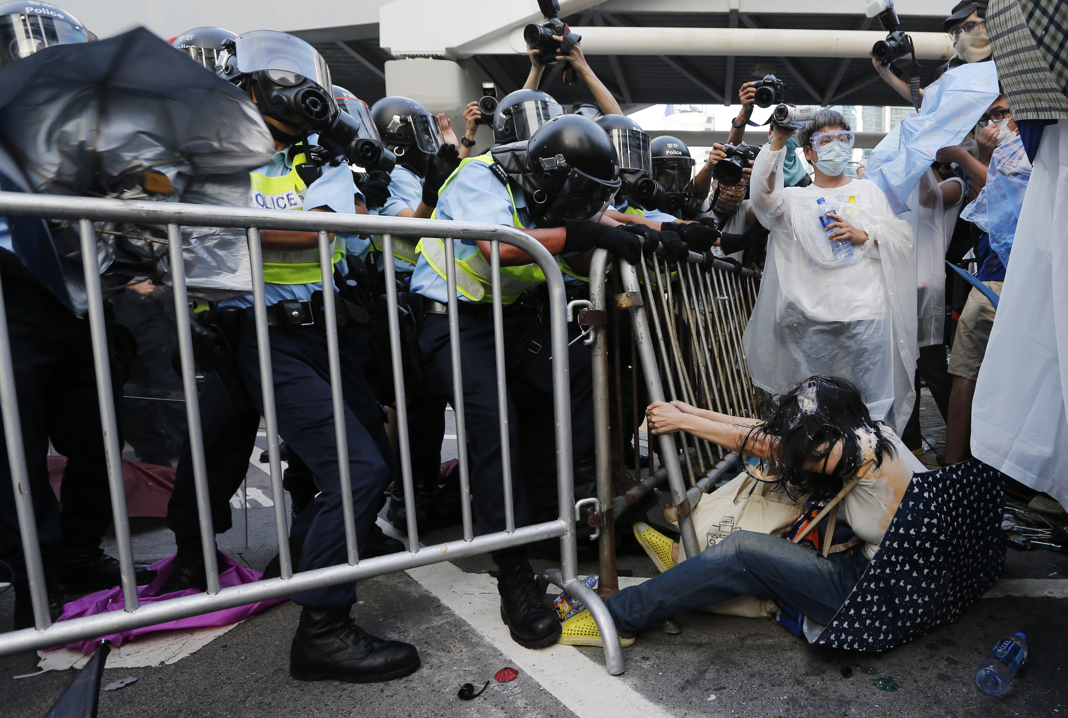 Woman on the ground holds on to a fence during a clash with riot policemen as tens of thousands of protesters block the main street to the financial Central district outside the government headquarters in Hong Kong