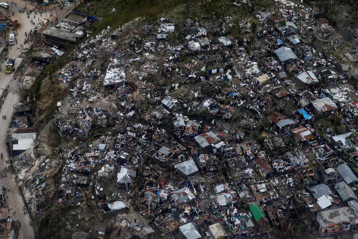 People wade through a flooded street and next to destroyed houses after Hurricane Matthew passes Jeremie