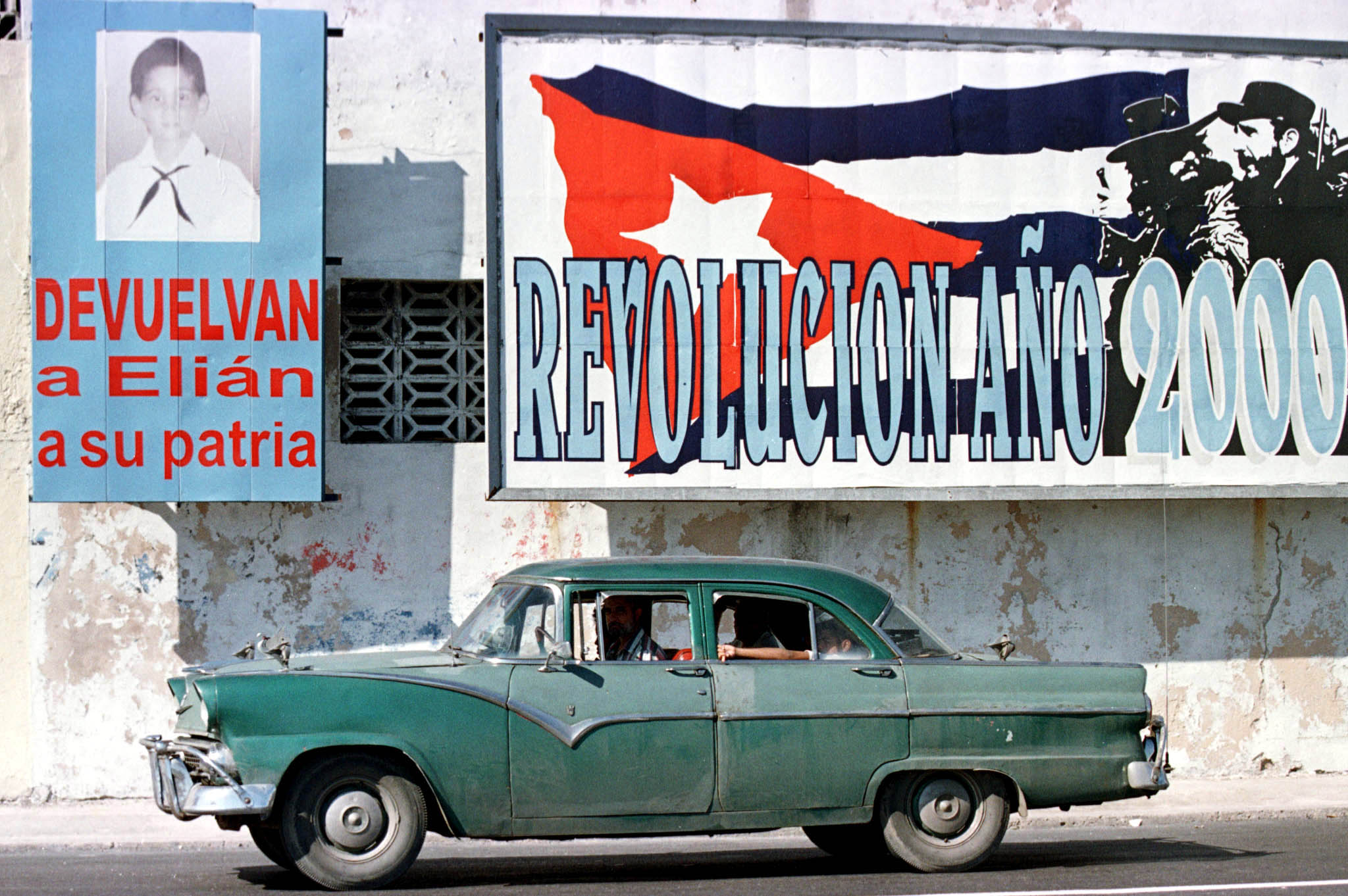 An old 1955 Ford drives past two billboards referring to Elian Gonzalez (L) which reads: "Return Eli..