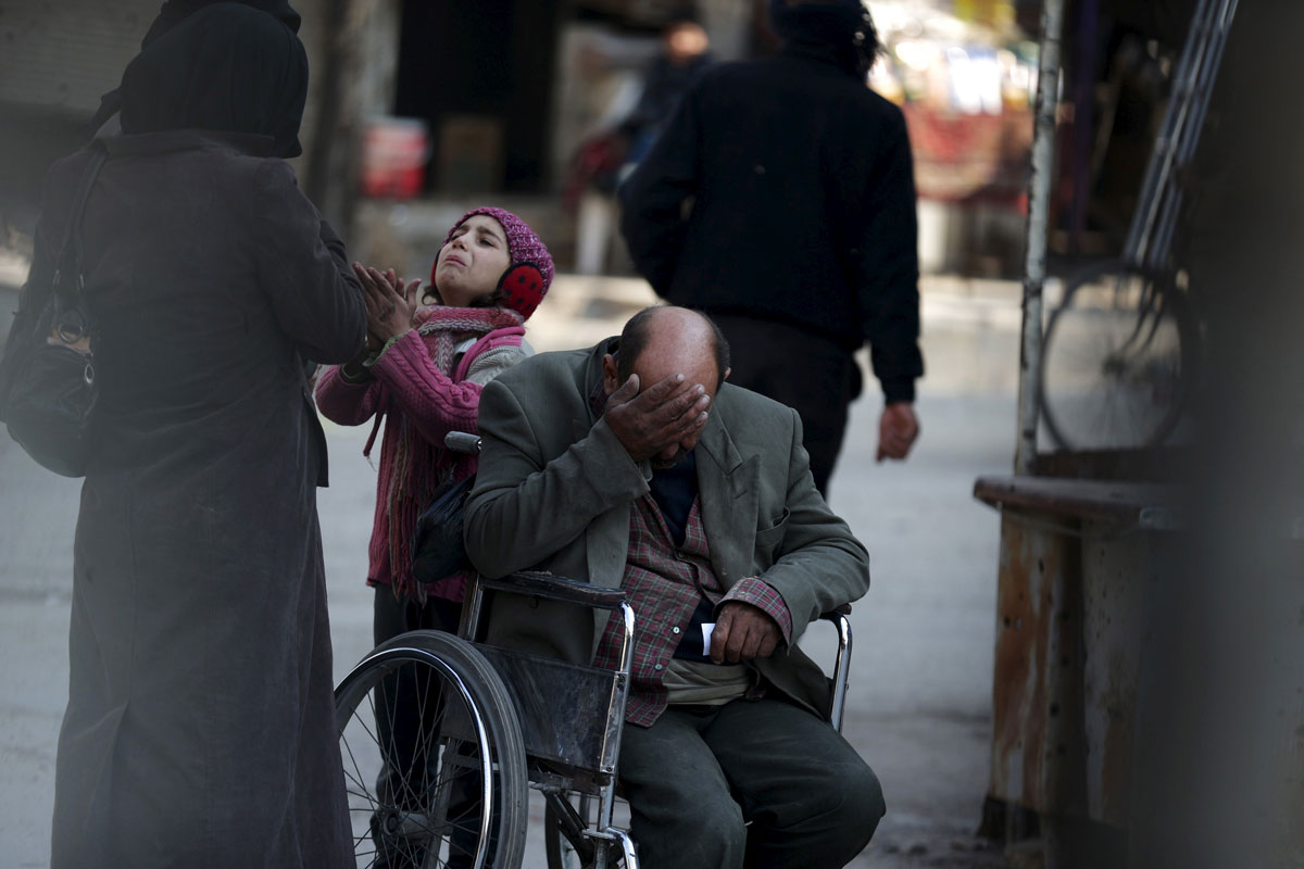 A girl with her father on a wheel chair, ask for help to pay a medical bill from passers by, in Douma, Syria