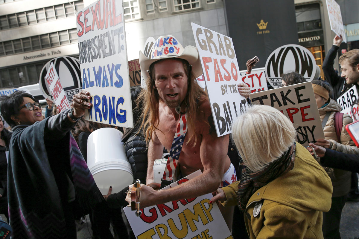 Women hold up signs as they surround Robert Burck, known as the "Naked Cowboy" who is a supporter of Republican U.S. presidential nominee Donald Trump as they protest against Trump in New York