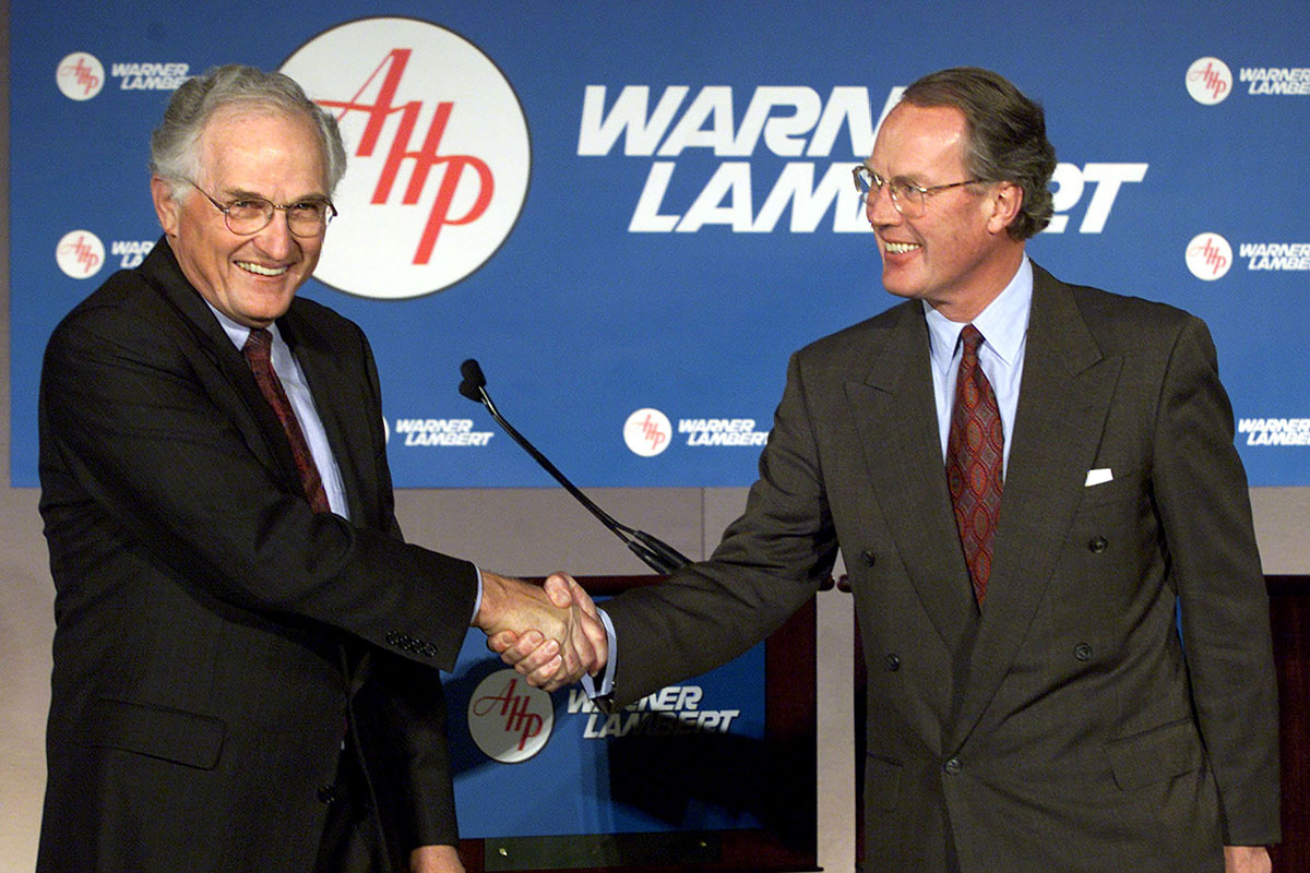 American Home Products Inc. Chairman and CEO John R. Stafford (L) shakes hands with Warner-Lambert C..