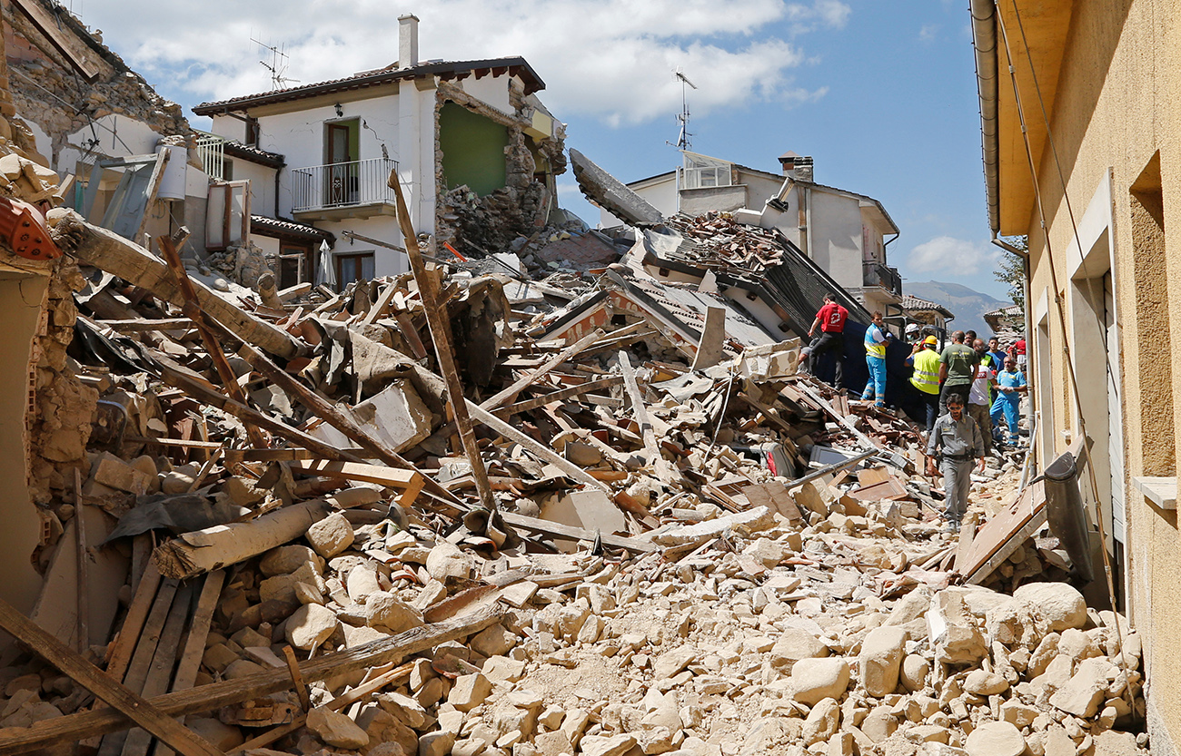 People and rescuers stand next collapsed buildings following an earthquake in Amatrice