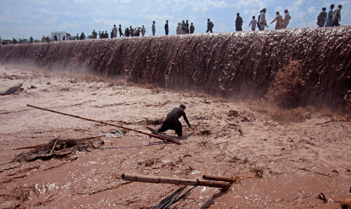 A shopkeeper tries to save belongings as residents use a bridge covered with floodwater after heavy rain in Nowshera District on the outskirts of Peshawar