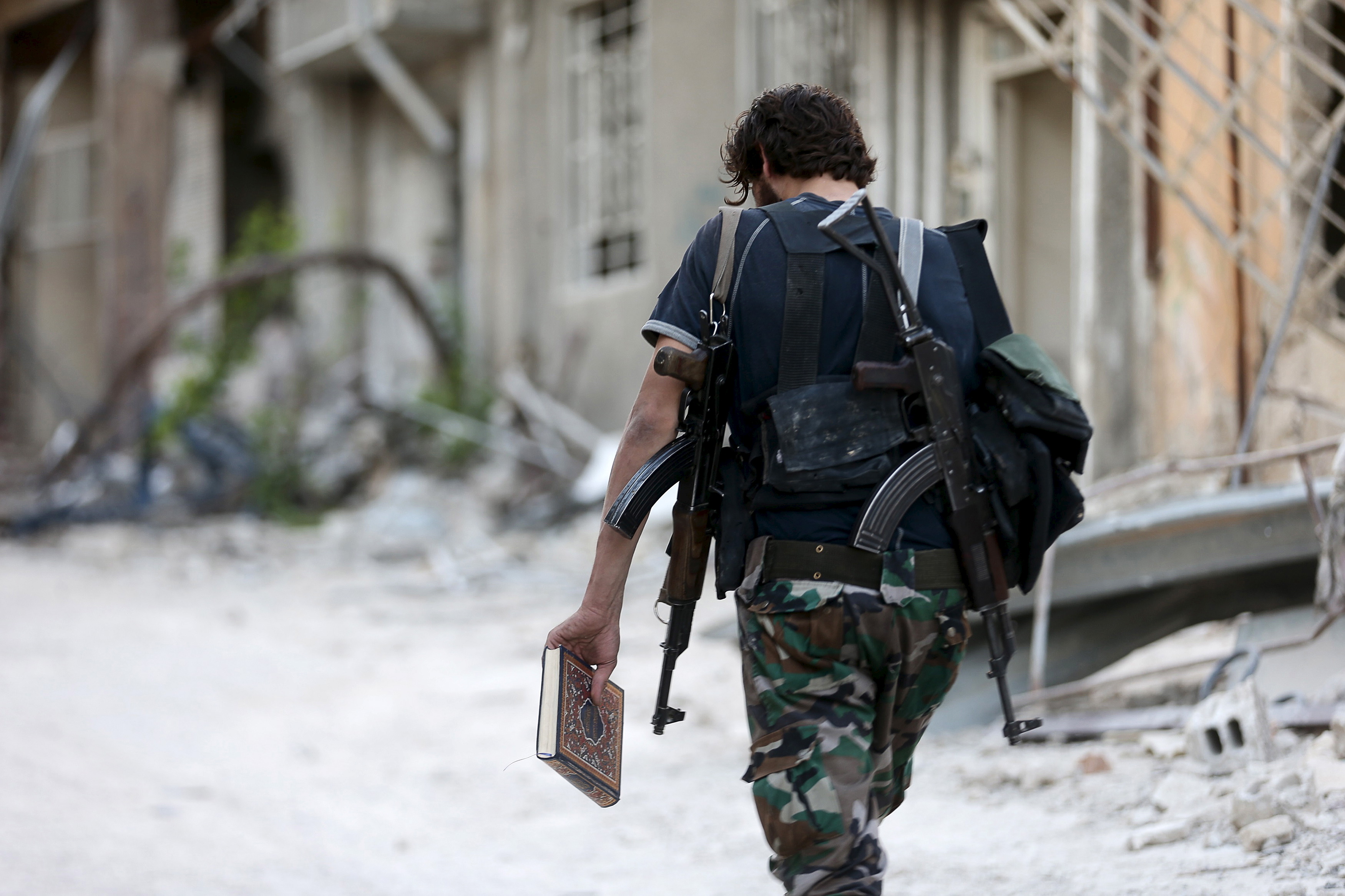 A Free Syrian Army fighter carries a copy of the Koran as he walks along a street in Jobar, a suburb of Damascus, Syria