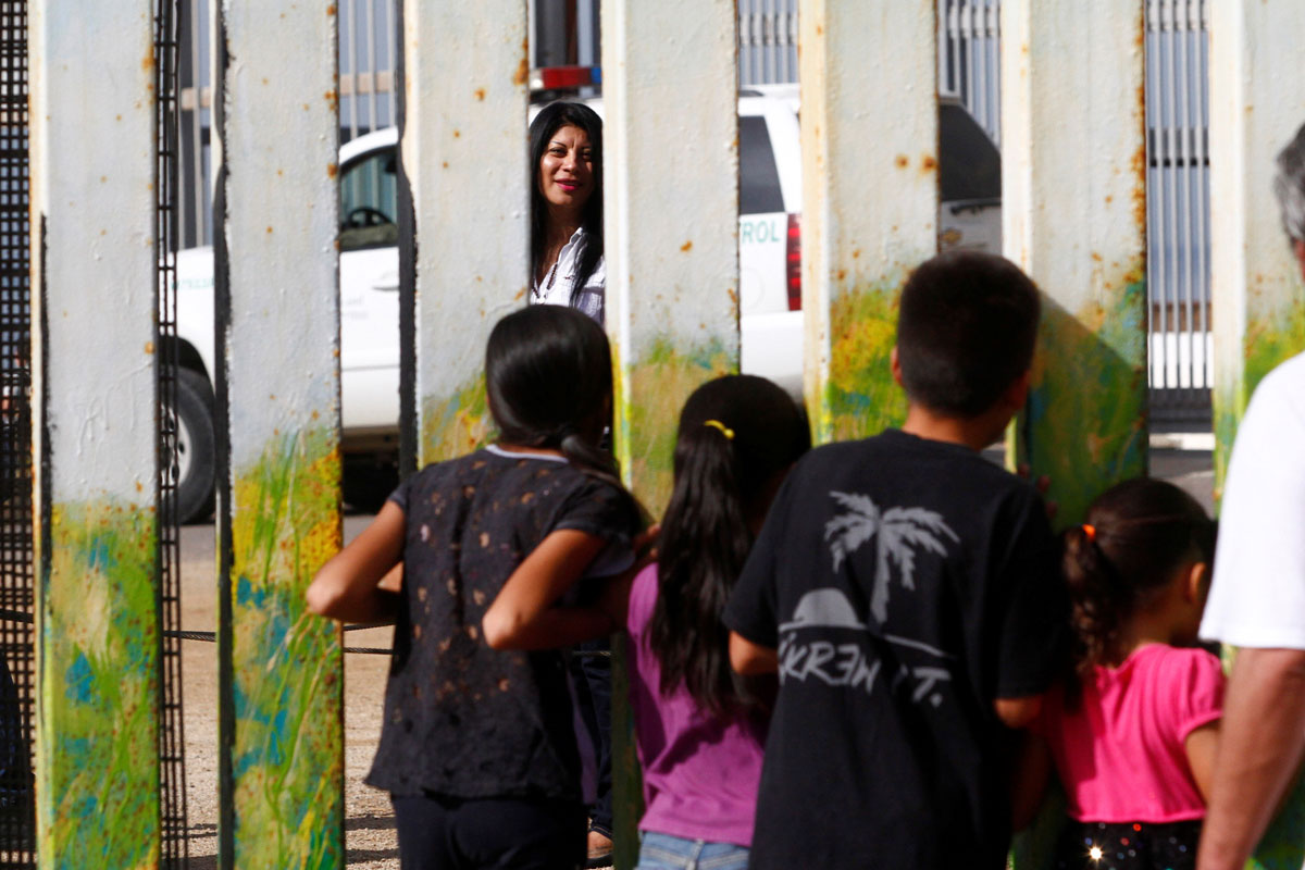 A woman speaks with children across a fence separating Mexico and the United States