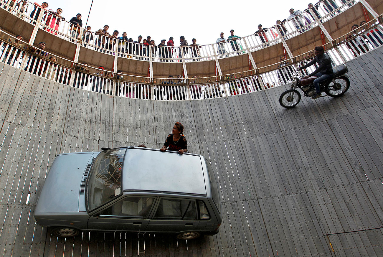 Stunt performers ride a motorcycle and a car on the walls of the "Well of Death" at the Magh Mela fair in Allahabad