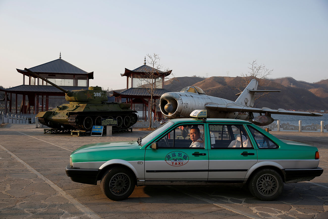 A taxi is parked in front of retired airplane and tank on display, at a Chinese village bordering North Korea at Dandong