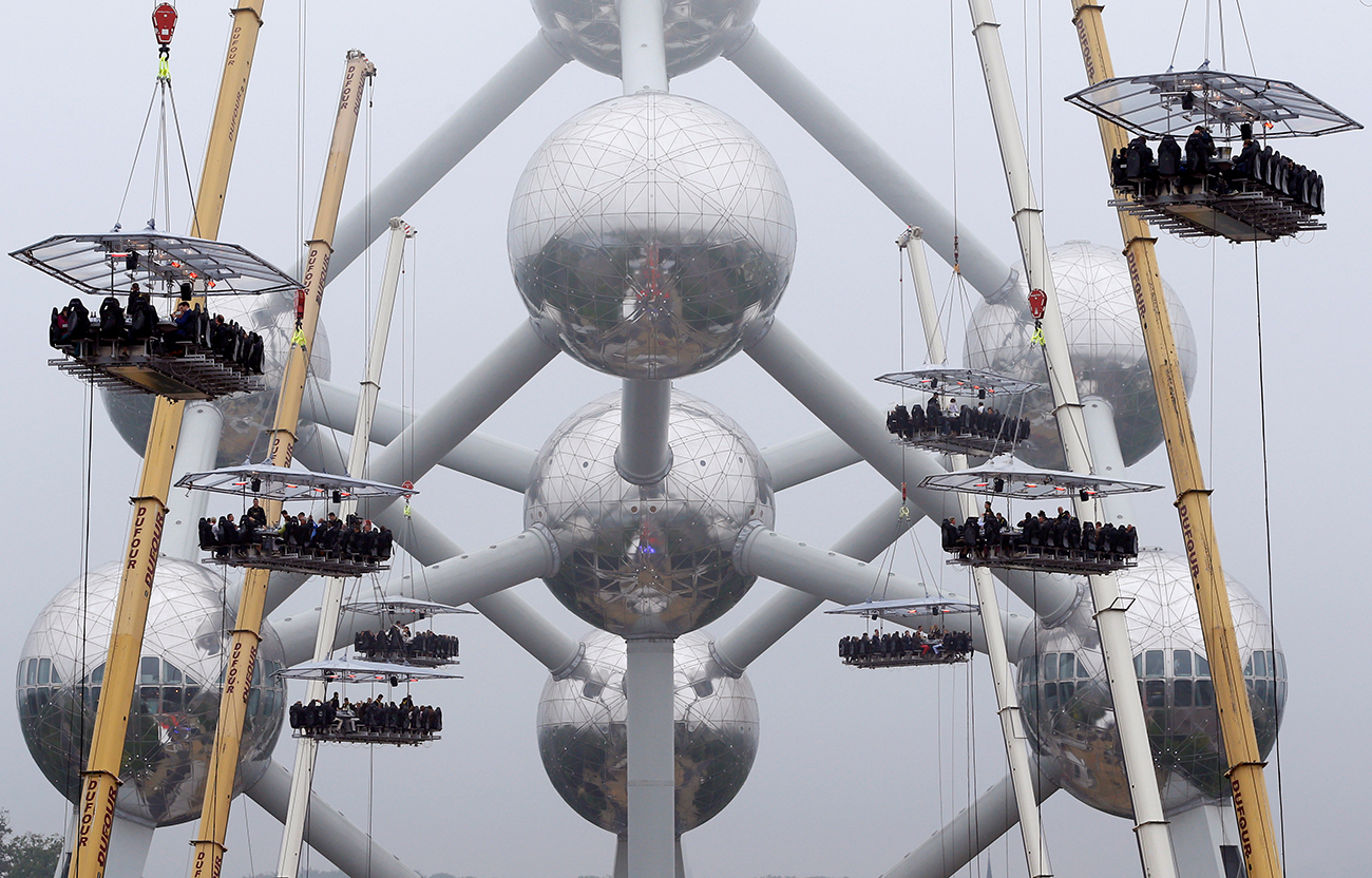 Guests sit at tables suspended from cranes at a height of 40 metres in front of the Atomium, as part of the 10th anniversary of the event known as "Dinner in the Sky", in Brussels