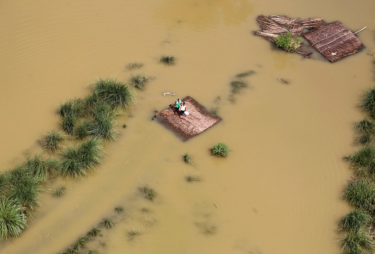 People stand on a partially submerged house as they wait to receive food parcels being distributed by a Indian Air Force helicopter on the outskirts of Allahabad