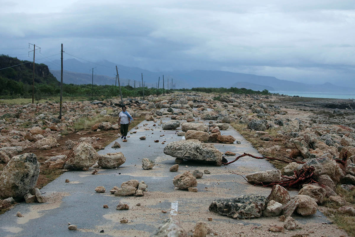 A woman walks on a highway blocked by rocks after the passage of hurricane Matthew on the coast of Guantanamo province