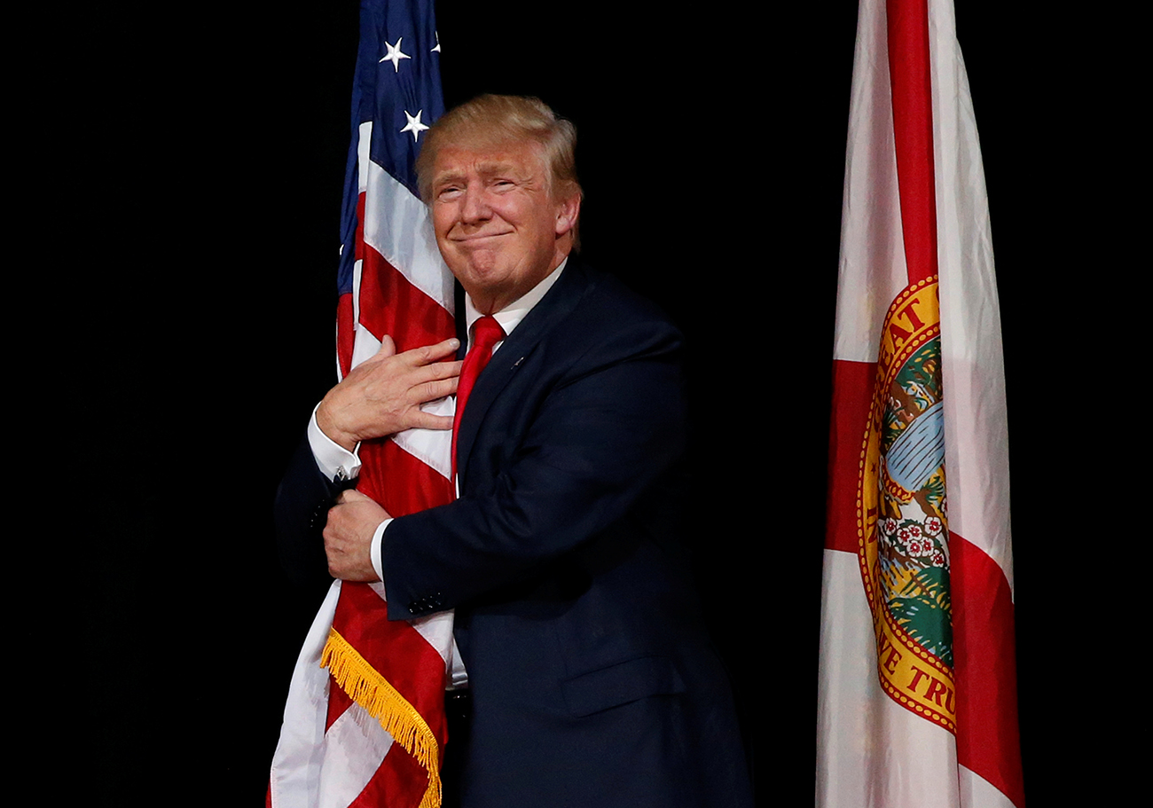 Trump hugs a U.S. flag as he comes onstage to rally with supporters in Tampa, Florida