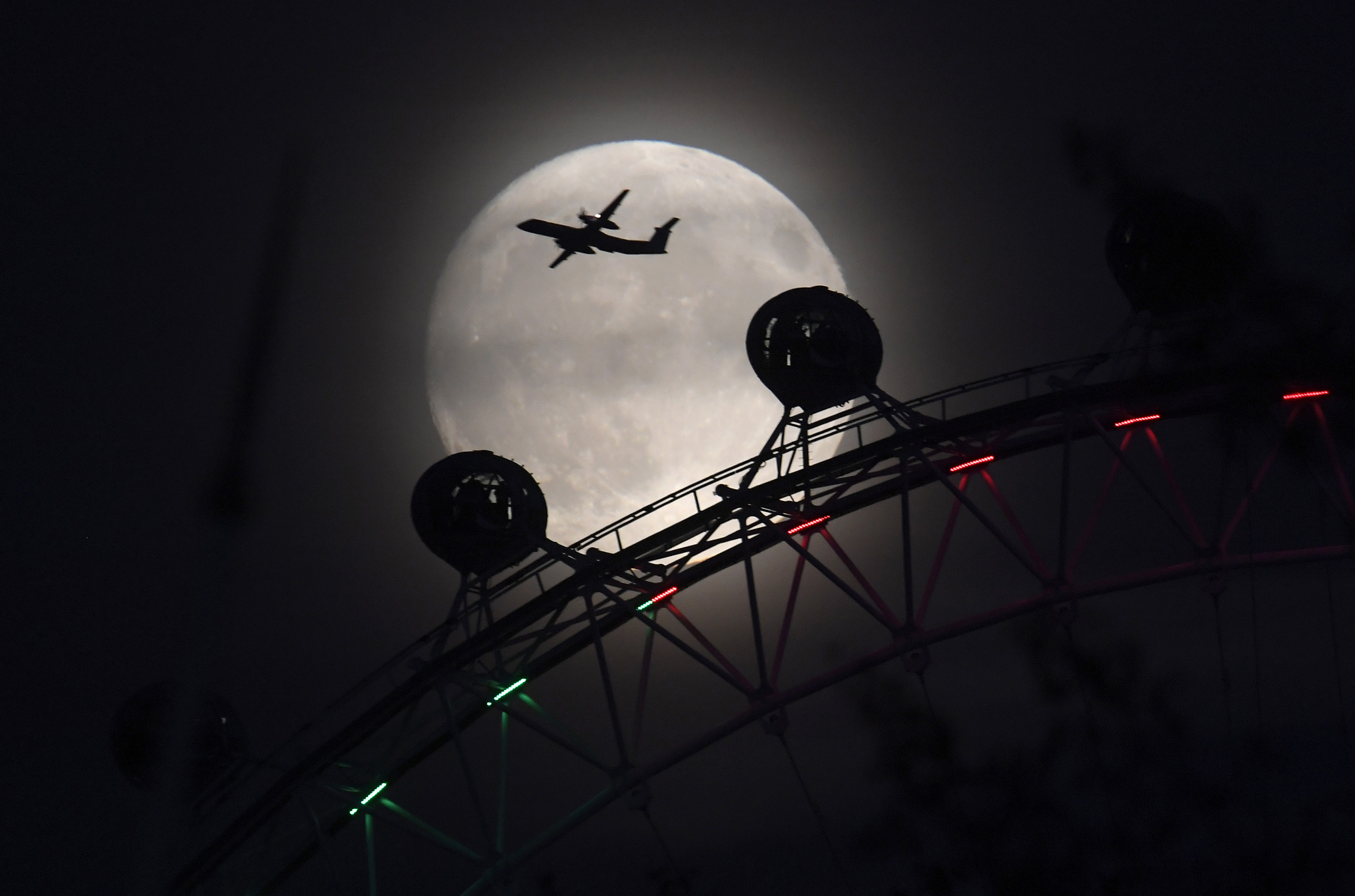 An aeroplane flies past the London Eye wheel, and moon, a day before the "supermoon" spectacle in London