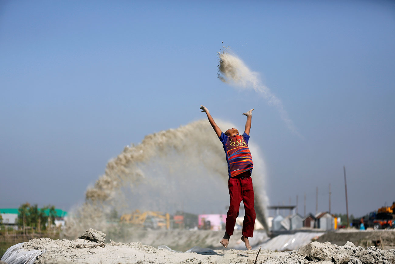 A boy plays with sand as his mother works in a nearby restaurant on the outskirt of Dhaka