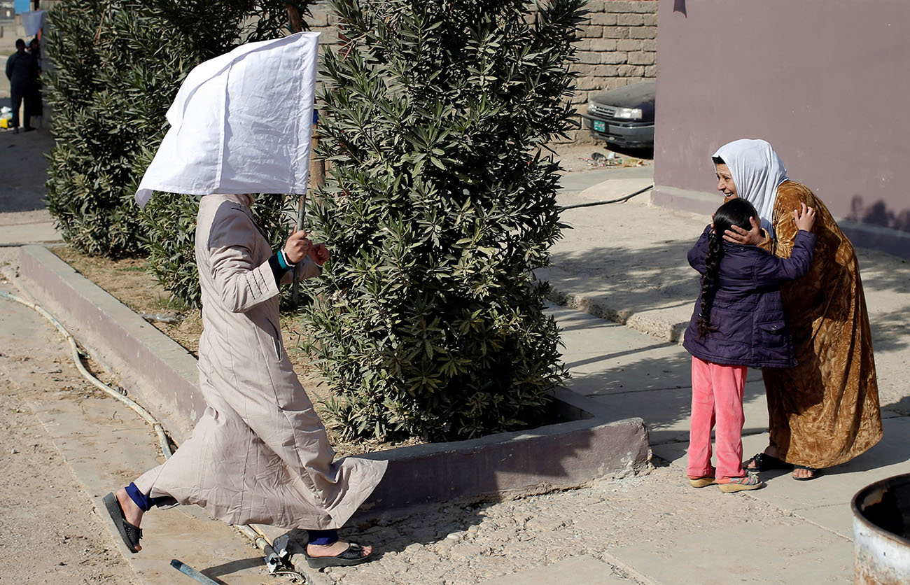 A woman holds up a white flag as she runs to greet her relative in Mosul