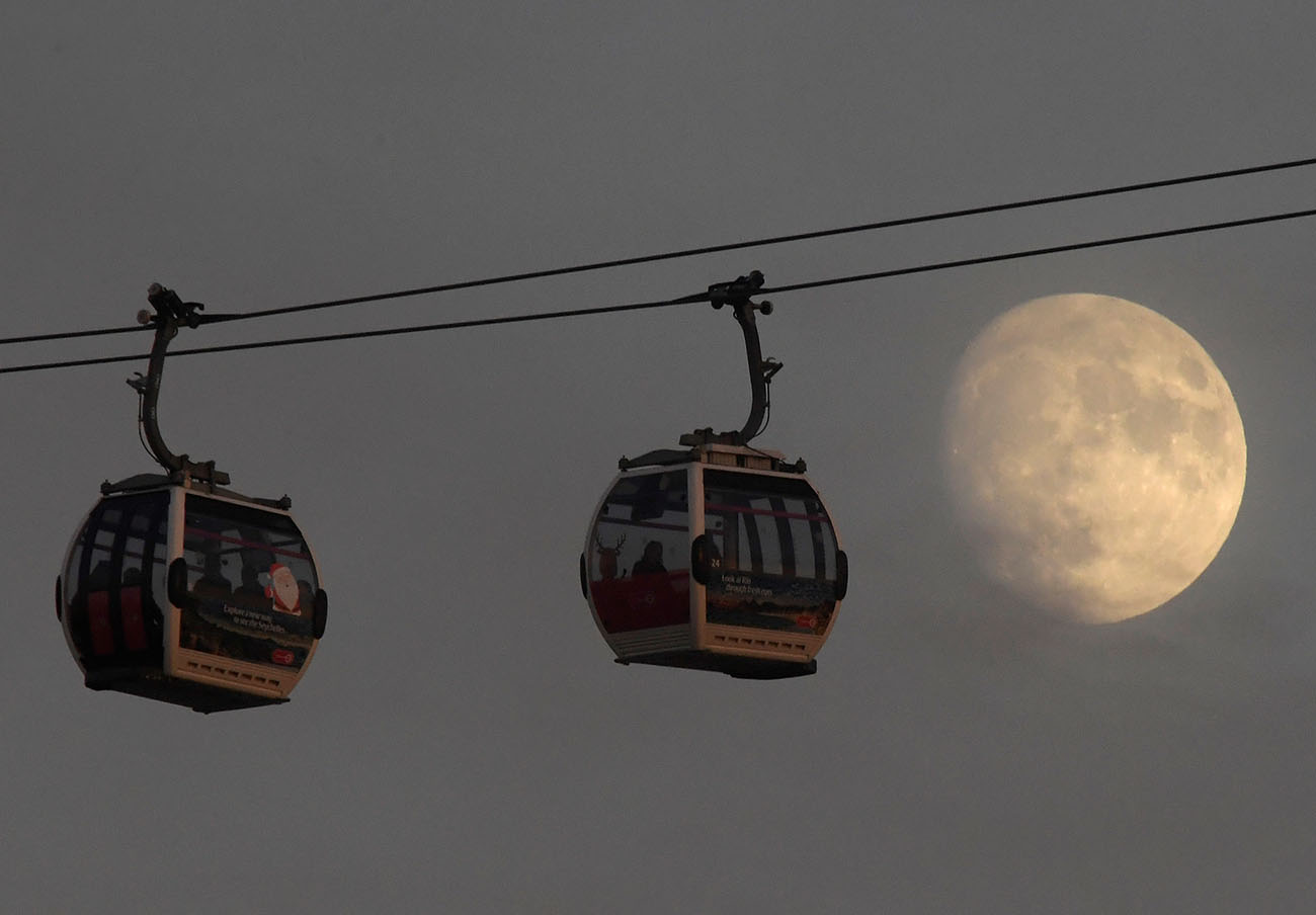 Passengers cross the River Thames in cable cars with the moon seen behind at Greenwich Peninsula in London