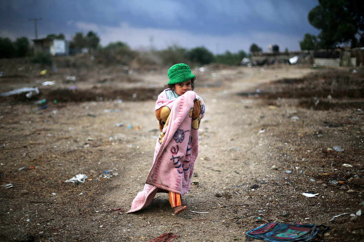 Palestinian girl, wrapped in a blanket, walks outside her family dwelling on a rainy day in Khan Younis in the southern Gaza Strip