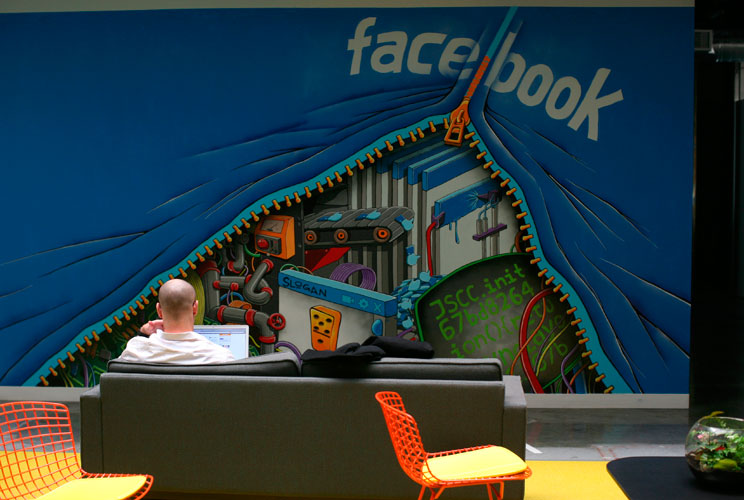 An employee works on a computer in front of a Facebook mural.  