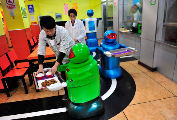 		<p>A robot that specialises in delivering food holds a tray as a waiter puts dishes on it at the Robot Restaurant.</p>