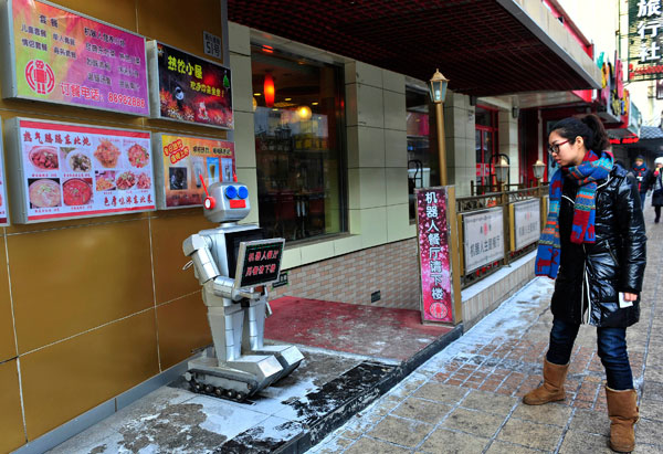 		<p>A pedestrian looks at a robot that specialises in greeting people outside the Robot Restaurant in Harbin, Heilongjiang province. The sign the robot is holding reads, "Robot Restaurant, go downstairs and have dinner."</p>