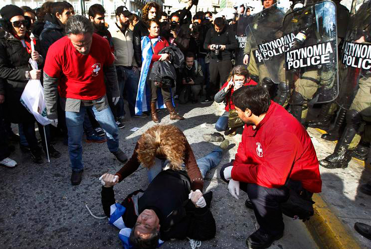 Medics try to help an anti-austerity protester, who lies unconscious after he was injured by police, in front of the parliament in Athens February 11, 2012, during a demonstration on the second day of a 48-hour strike by Greek workers unions.