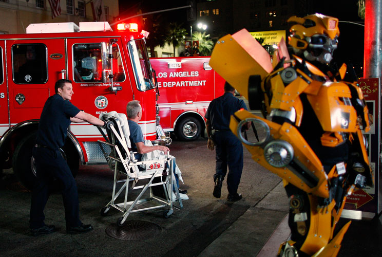 A man with an unknown medical problem is wheeled to an ambulance past Jay Netka, a Hollywood superhero impersonator who is wearing a costume that he made of Bumble Bee, near the site of the 84th Oscars.