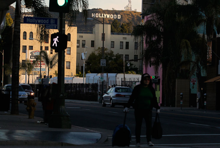 A women walks with her belongings under the Hollywood sign and across Hollywood Boulevard.