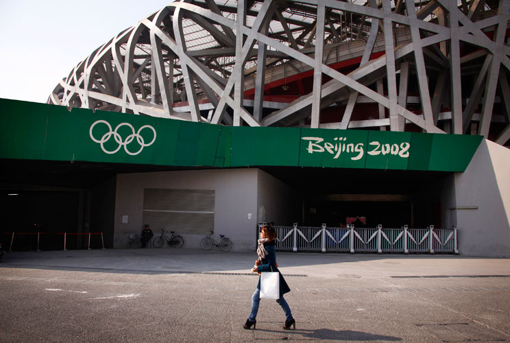 A woman walks past a security guard outside the National Stadium, also known as the "Bird's Nest", which was the venue for the athletics and the opening and closing ceremonies of the 2008 Olympic Games in Beijing March 23, 2012. The gigantic infrastructur