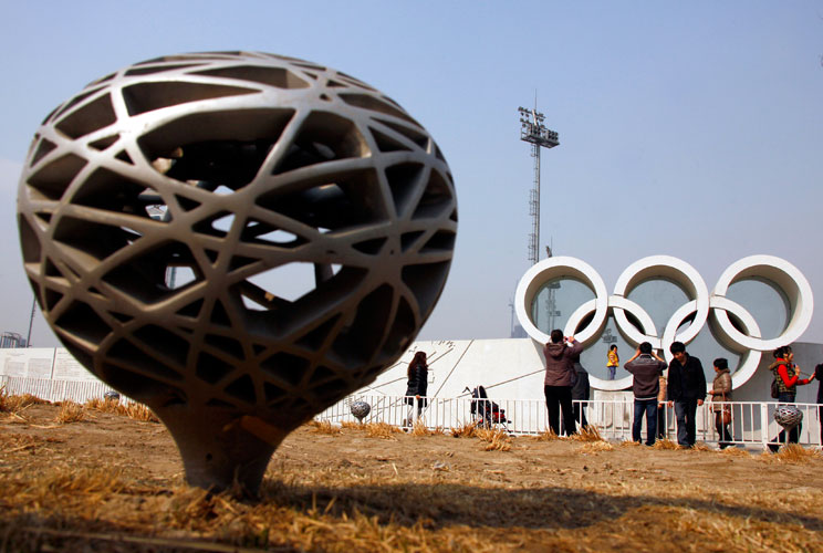 Tourists pose for photographs on cement Olympic rings next to a lamp resembling the National Stadium, also known as the "Bird's Nest", in the former Olympic Green area in Beijing March 23, 2012. The gigantic infrastructures built for the Beijing Olympics,