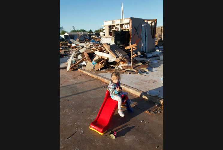 Edie Paroish, 3, plays on a slide in front of a destroyed home following a tornado that struck the town.