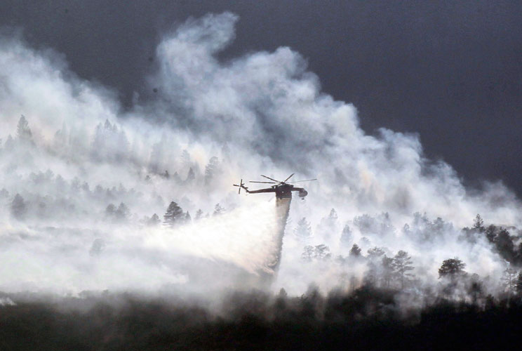 A helicopter drops water on the Waldo Canyon fire burning behind the U.S. Air Force Academy, west of Colorado Springs, Colorado, on June 27, 2012. Firefighters struggled Wednesday to beat back a wildfire raging at the edge of Colorado Springs that doubled