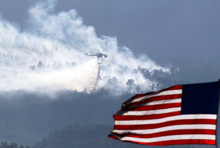 A helicopter drops water on the Waldo Canyon fire burning behind the U.S. Air Force Academy, west of Colorado Springs, CO, June 27, 2012. Firefighters struggled on Wednesday to beat back a wildfire raging at the edge of Colorado Springs that doubled in si