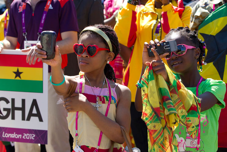 Children take photos of performers with their mobile phones as members of Ghana's Olympic squad arrive in the Athletes Village at the Olympic Park in London July 24, 2012. REUTERS/Neil Hall (BRITAIN - Tags: SPORT OLYMPICS)