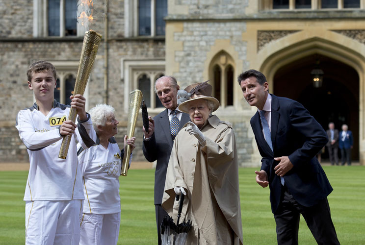 Britain's Queen Elizabeth (2nd R), Prince Philip (C), LOCOG Chairman Sebastian Coe (R) and Olympic torch bearer Gina Macgregor (2nd L) watch as torchbearer Phil Wells takes the Olympic Flame at Windsor Castle, west of London, July 10, 2012. REUTERS/Ben St