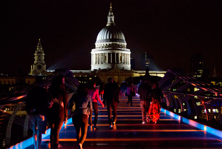 People walk on Millenium Bridge as it is lit up to celebrate the Olympics in London July 21, 2012. St. Paul Cathedral is seen in the background. REUTERS/Neil Hall (BRITAIN - Tags: SPORT OLYMPICS CITYSPACE)