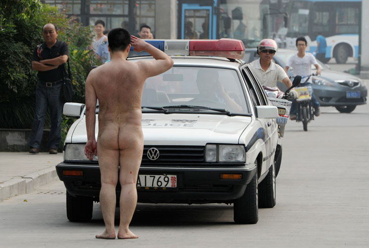 A naked man salutes a police vehicle in the middle of a street in Hefei, Anhui province July 17, 2012. The man ran onto a busy street on Tuesday morning wearing only a pair of shorts, climbing onto cars and smashing windows with his bare fists. He was tak