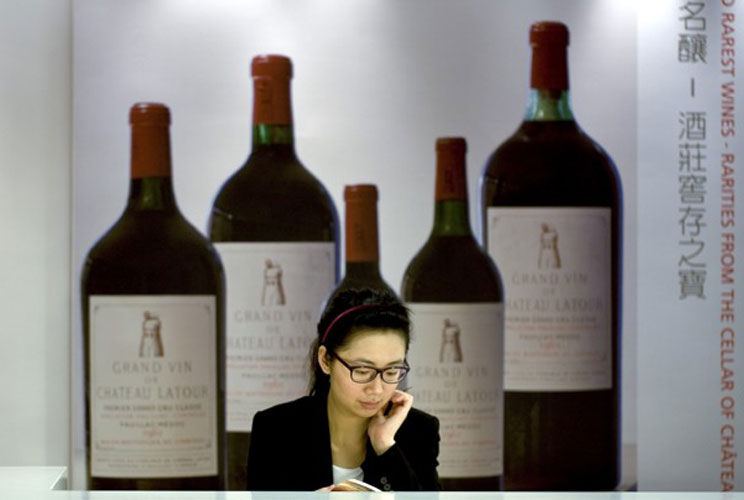 A Christie’s staff member sits near an advertisement for Chateau Latour fine wines for auction in Hong Kong. Chinese buyers spent $106 million on vintage bottles of Chateau Latour and modern paintings at the start of a week-long Hong Kong auction.