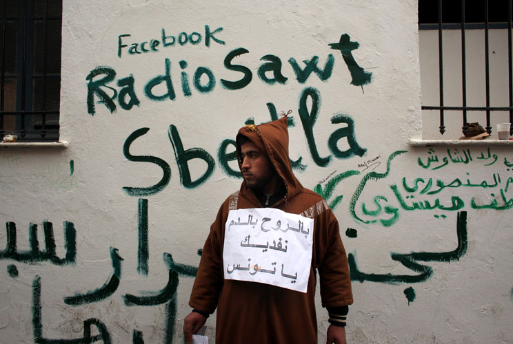 A man stands next to Facebook graffiti as Tunisians continued their demonstrations outside Prime Minister Mohammed Ghannouchi's offices in Government Square Tunis on January 25, 2011 in Tunis, Tunisia. The government square became a makeshift camp as prot