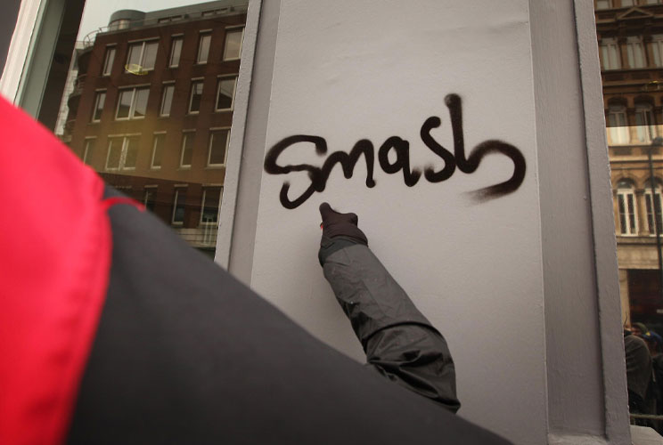 A protestor uses a can of spray paint at a bank as violence breaks out during a march in protest at government cuts on March 26, 2011 in London, England. Thousands took part in the Trades Union Congress (TUC) organised march to Hyde Park. 