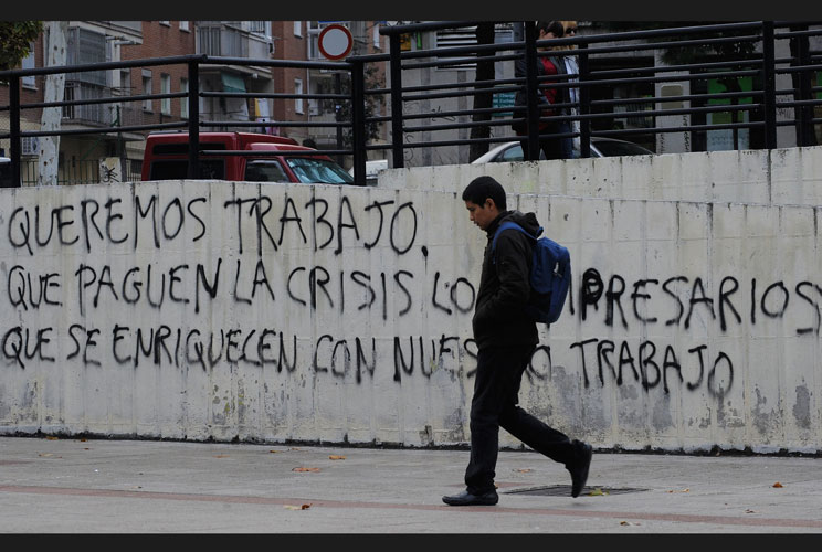 A youth walks past graffitti which reads 'We want to work, let the businessmen who have got rich from our labour pay for the crisis' on November 10, 2011 in Madrid, Spain. The current Eurozone debt crisis has left Spain with crippling economic problems. M