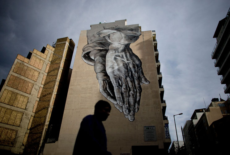 A man walks past graffiti displayed on a building on December 6, 2011 in Athens, Greece. Graffiti artists throughout the city are expressing the effects of austerity measures that have plagued the community as Greece continues to struggle in debt while la