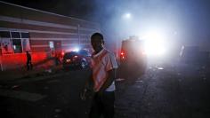 A protester walks through the smoke of burning Baltimore buildings set ablaze by rioters, as a police armored car drives past, during clashes in Baltimore