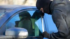 A thief using a metal rod to unlock the front door of a car